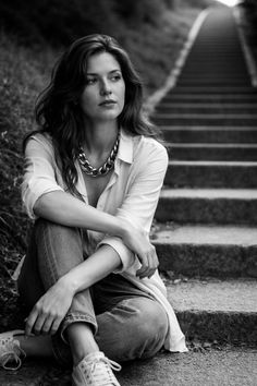 Woman with long hair and a chunky necklace sitting on outdoor stairs