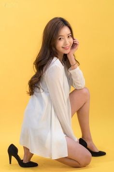 Woman in a white dress and black heels kneeling on a yellow background