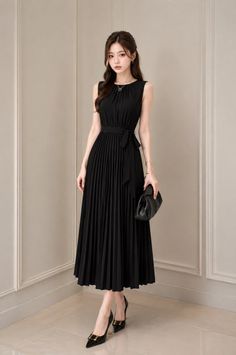Woman in a black pleated dress and high heels holding a clutch bag indoors