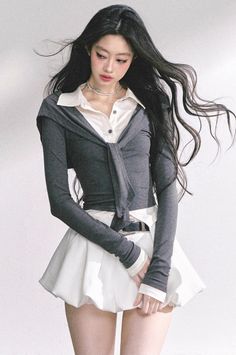 Woman with long black hair wearing a white shirt and gray cardigan over a white skirt