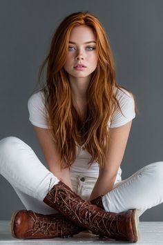 Woman with long red hair and blue eyes wearing a white t-shirt and brown boots