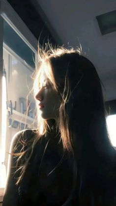 Woman with long hair looking out a window with strong backlight