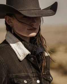Woman in a cowboy hat and denim jacket with windblown hair outdoors