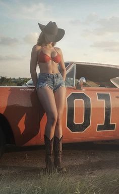 Woman in a cowboy hat, red bikini top, and denim shorts leaning on an orange car
