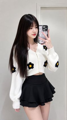 Woman with long black hair taking a mirror selfie in a white cardigan and black skirt