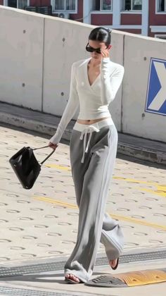 Woman in a white top and gray pants walking outdoors with a black handbag
