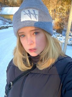 Young woman with blonde hair and blue eyes wearing a winter hat and puffer jacket in the snow