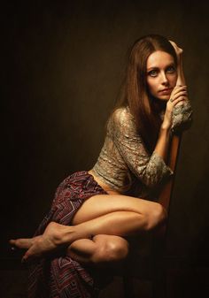 Woman with long hair in a lace top and patterned skirt, sitting with exposed legs