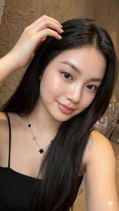 Woman with long black hair wearing a black top and a clover necklace