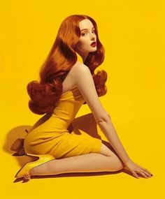 Woman with long red hair in a yellow dress and heels against a bright yellow background