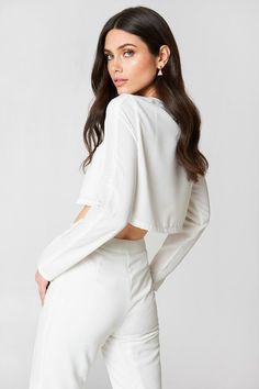 Woman in a white crop top and high-waisted pants looking over her shoulder