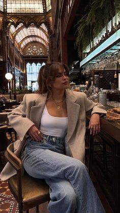Woman in a blazer and jeans sitting at a bar indoors