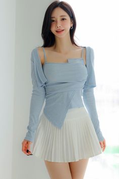 Woman with long dark hair wearing a light blue top and white pleated skirt indoors