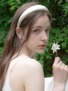 Woman with long hair and a white headband holding a white flower outdoors