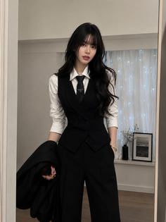 Woman in a black suit and white shirt with a black tie indoors