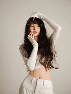 Woman with long dark hair and glasses wearing a white crop top and pants