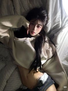 Woman with long dark hair in a hoodie and shorts lying on a bed