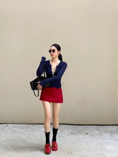 Woman in a red mini skirt and long sleeve top with a black handbag