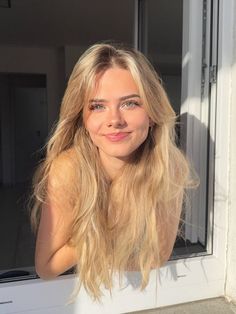 Young woman with blonde hair looking out a window in golden hour light