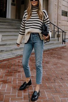 Woman in a striped sweater, blue jeans, and black loafers on a brick pavement