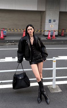 Woman in a black leather jacket and mini skirt leaning on a railing on a street