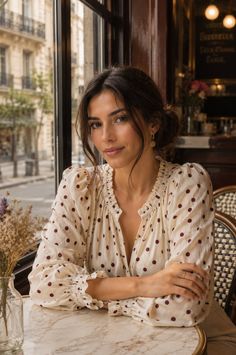 Woman in a polka dot blouse sitting at a cafe table