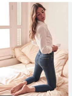 Woman in a white shirt and blue jeans kneeling on a bed