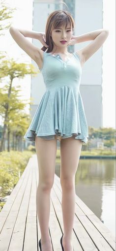 Woman in a light blue dress posing outdoors with hands behind her head