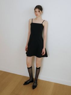 Woman in a black dress and knee-high socks standing against a white wall