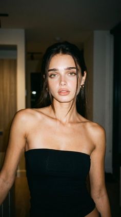 Woman with dark hair and green eyes wearing a black tube top indoors