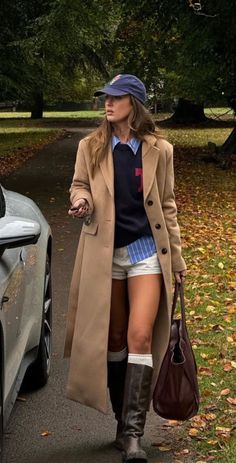 Woman in a long coat, shorts, and boots walking outdoors with autumn leaves