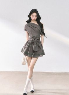 Woman with long black hair wearing a gray one-shoulder dress and white socks