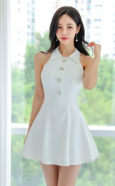 Woman in a white halter dress with pearl earrings standing indoors