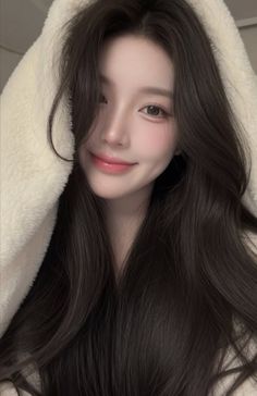 Woman with long dark hair wearing a white fluffy hoodie, smiling softly