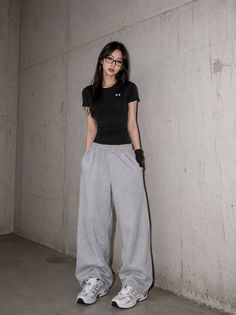 Woman with long hair and glasses wearing a black t-shirt and sweatpants indoors