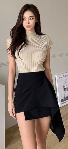 Woman with long dark hair wearing a ribbed top and black asymmetrical skirt indoors