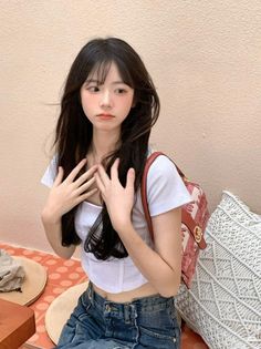 Young woman with long black hair wearing a white crop top and jeans indoors