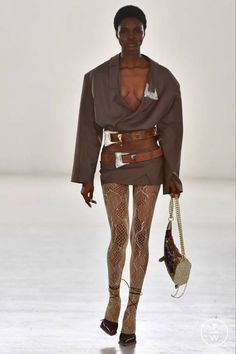 Model in an oversized blazer, mini skirt, and snakeskin tights on a runway