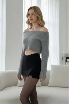 Woman with blonde hair wearing an off-shoulder crop top and black skirt with tights