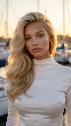 Blonde woman with long wavy hair in a white top at golden hour in a marina