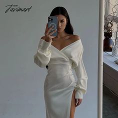 Woman in a white off-shoulder dress with a high slit taking a mirror selfie