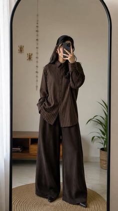 Woman in a striped shirt and wide leg pants taking a mirror selfie