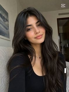 Woman with long dark hair wearing a black top and necklace indoors