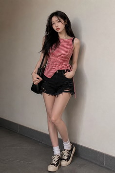 Woman with long dark hair wearing a red gingham top and ripped shorts