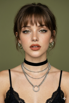 Woman with bangs, a septum ring, and layered chain necklaces over a black lace top