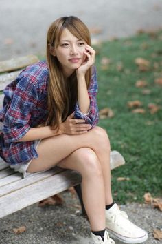 Woman with long hair wearing a plaid shirt and shorts sitting on a park bench