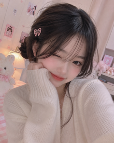Woman in a white sweater winking with a pink bow in her hair