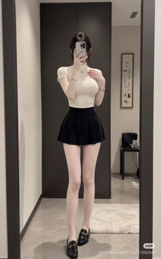 Woman in a black pleated skirt and white turtleneck taking a mirror selfie