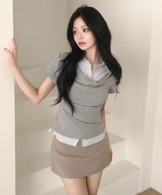 Woman with long black hair wearing a grey top and mini skirt indoors