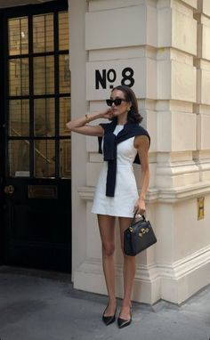 Woman in a white dress and black sweater posing on a street